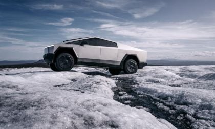 Tesla Cybertruck in stainless steel parked on an icy ridge, showcasing its angular design, off-road tires, and futuristic exterior in a cold landscape.