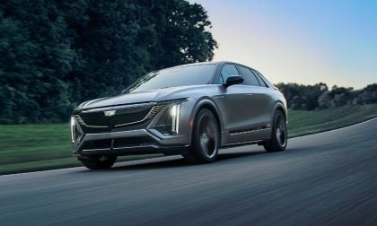 Silver 2026 Cadillac Lyriq electric SUV curving on a road with green trees and blurred motion
