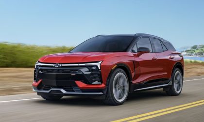 A sleek red Chevrolet SUV drives along a scenic road, showcasing bold design and modern features against a clear blue sky.