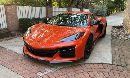 Orange sports car parked on a driveway, surrounded by brick walls and greenery.