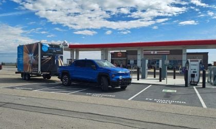 Blue electric truck with a trailer parked at an EV charging station near a convenience store.