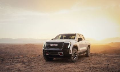 White GMC pickup truck parked on a rocky hilltop at sunset with mountains in background.