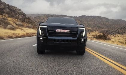 Black GMC pickup truck, front view on desert highway, featuring LED headlights, bold grille, rocky mountain landscape background.