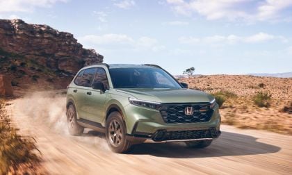 Green Honda CR-V SUV driving on dusty desert road with rocky cliff backdrop