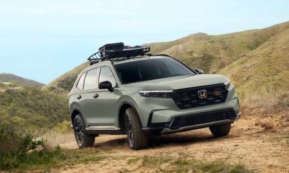 Green Honda CR-V SUV kicking up dust while driving on desert road with rocky cliff backdrop