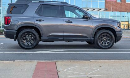 2026 Honda Passport TrailSport Elite in gray shown in full side profile parked on a city street with modern buildings in the background.