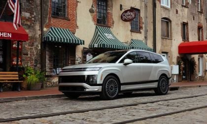 A sleek silver electric SUV parked on cobblestone streets, beside charming brick buildings and awning-covered shops.