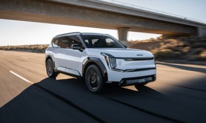 White 2026 Kia EV9 SUV driving under highway overpass, angular design with dynamic motion blur