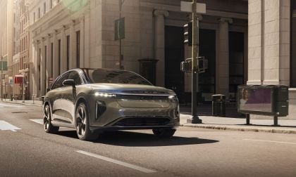 Silver electric SUV driving on urban street with classical architecture and morning sunlight