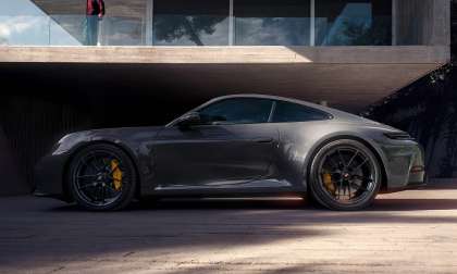 Gray 2026 Porsche 911 Carrera parked outside a modern home with large yellow brake calipers and black wheels.