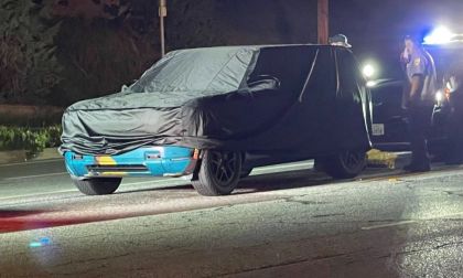 2026 Rivian R2 electric SUV front three-quarter view in colorful camouflage wrap driving on city street at night.