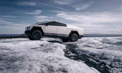 Tesla Cybertruck positioned on icy terrain, side profile view emphasizing stainless steel exterior, rugged tires, and electric truck capability in extreme conditions.