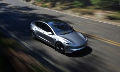 A silver Tesla Model 3 Performance speeds down a winding road, surrounded by lush greenery, showcasing its sleek design and dynamic motion.