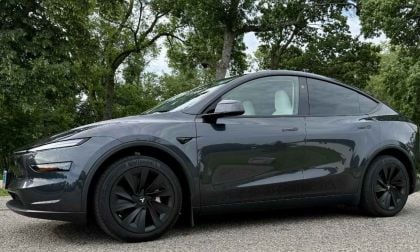 Dark gray Tesla Model Y Performance SUV parked on asphalt with lush green trees in background