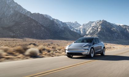 Photograph of a 2026 Tesla Model Y electric SUV in the Juniper color, shown from a three-quarter front angle with the vehicle's front grille, headlights, and side profile clearly visible against a plain background.