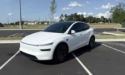 A white electric car parked in a sunny lot, featuring sleek lines, tinted windows, and black rims amidst a clear blue sky.