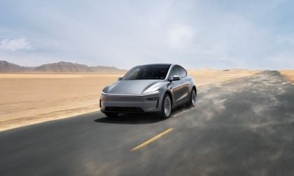 Silver 2026 Tesla Model Y driving on desert road with mountains, dynamic motion blur showing speed and movement
