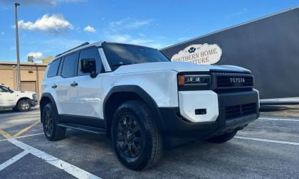 2024 Toyota Land Cruiser in pearl white, front three-quarter view, featuring black wheels and trim, parked outside Southern Home Furniture store.