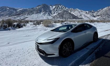 2026 Toyota Prius hybrid front three-quarter view in white driving through snowy mountain landscape