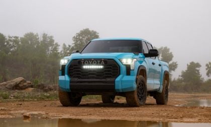 A bright blue 2026 Toyota Tundra TRD Pro is shown from a front three-quarter angle, positioned on muddy terrain with its LED lights illuminated and distinctive black grille prominently displayed.