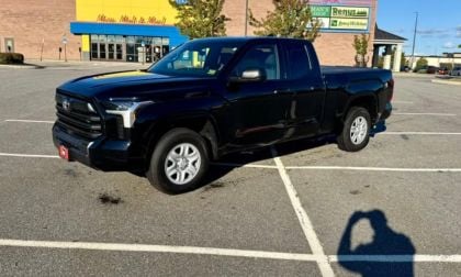 Black pickup truck parked in a lot near a shopping center on a sunny day.