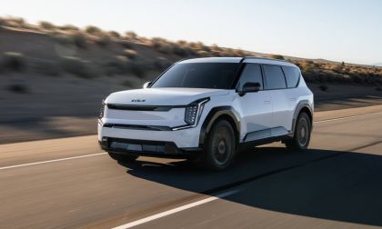 A sleek white Kia electric SUV driving on a desert road, showcasing its modern design and aerodynamic features under a clear sky.