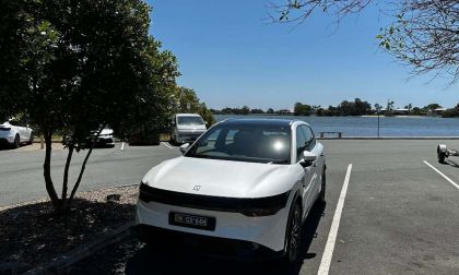 White car parked in a lot near a lake, surrounded by trees and other vehicles.