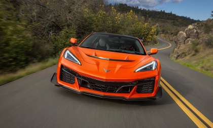 Orange 2026 Chevrolet Corvette ZR1X driving toward the camera on a winding two-lane road.