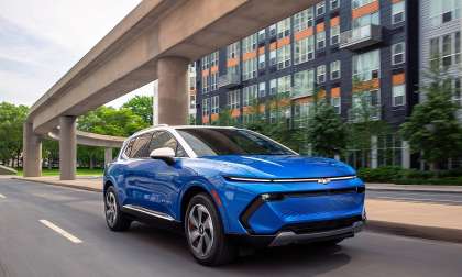 Blue 2026 Chevrolet Equinox EV LT driving through a city street, shown from the front three-quarter angle.