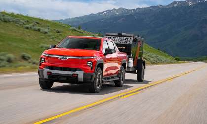A red Chevrolet Silverado EV Trail Boss towing a small trailer on a mountain highway.