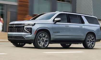 Grey 2026 Chevrolet Suburban driving through a city street with Chevrolet’s updated front-end styling.