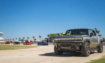 GMC Hummer EV parked at a racetrack with several supercars driving in the background.