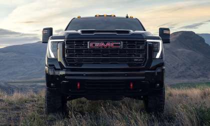 2026 GMC Sierra 2500 HD AT4 shown from the front on a grassy overlook with mountains in the background.