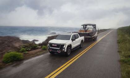 White 2026 GMC Sierra EV AT4 towing a boat along a misty coastal highway.