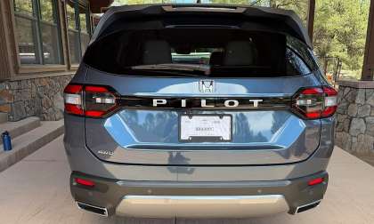 Rear view of a blue-gray 2026 Honda Pilot AWD parked under a covered driveway near a cabin.