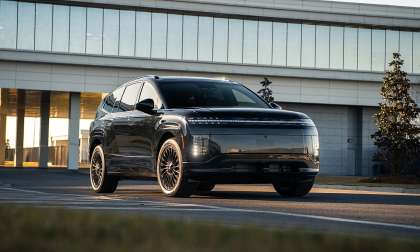 Black 2026 Hyundai Ioniq 9 driving past a modern building in a front three-quarter action shot.