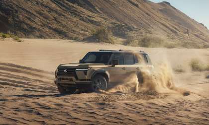 Lexus GX driving through deep sand with dust spraying around the SUV.