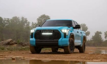 A head-on shot of a light blue 2025 Toyota Tundra TRD Pro with its distinctive LED light bar turned on, parked in a muddy, off-road environment.