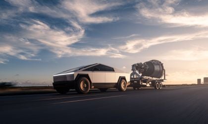 Tesla Cybertruck stainless steel electric pickup towing a large trailer on a highway at sunset