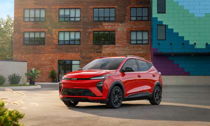 Red 2027 Chevrolet Bolt parked in front of a colorful urban building.