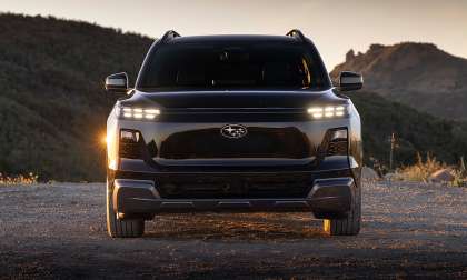 Front view of a black 2027 Subaru Getaway parked on a dirt overlook at sunset with mountains in the background.