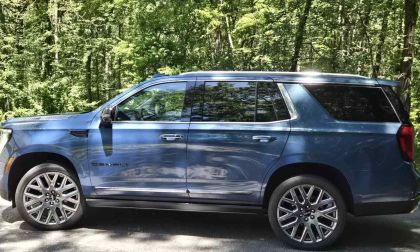 Blue 2025 GMC Yukon Denali SUV parked on asphalt with lush green forest background