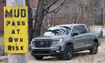 A 2026 Honda Ridgeline passes by a sign warning of mud hazard on a dirt road