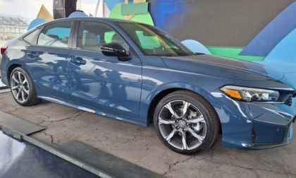 A dark blue 2025 Honda Civic is showcased indoors on a concrete surface. The car features modern design elements and curved lines, conveying a sense of elegance.