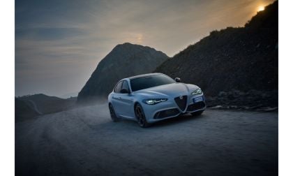 Alfa Romeo driving on misty mountain road at dramatic sunset with rocky landscape