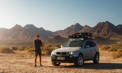 BMW x3 in Desert, person standing next to it with mountains in background