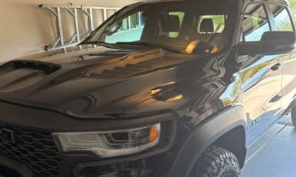 A shiny black 2025 Ram 1500 RHO is parked in a garage reflecting sunlight. Its aggressive design is accentuated by bold headlights and a textured hood.
