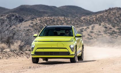A vibrant green 2025 Hyundai Kona EV drives along a dusty road, surrounded by rugged hills and a cloudy sky.