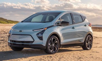 Chevrolet Bolt EV electric hatchback parked on a beach with ocean and sand dunes in the background.
