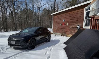 Chevrolet Equinox EV parked outside house connected to portable solar panels in snow